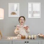 A child joyfully paints Easter eggs indoors, surrounded by lamps and art.