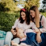 Three women enjoying a happy picnic outdoors in summer, laughing and relaxing together.