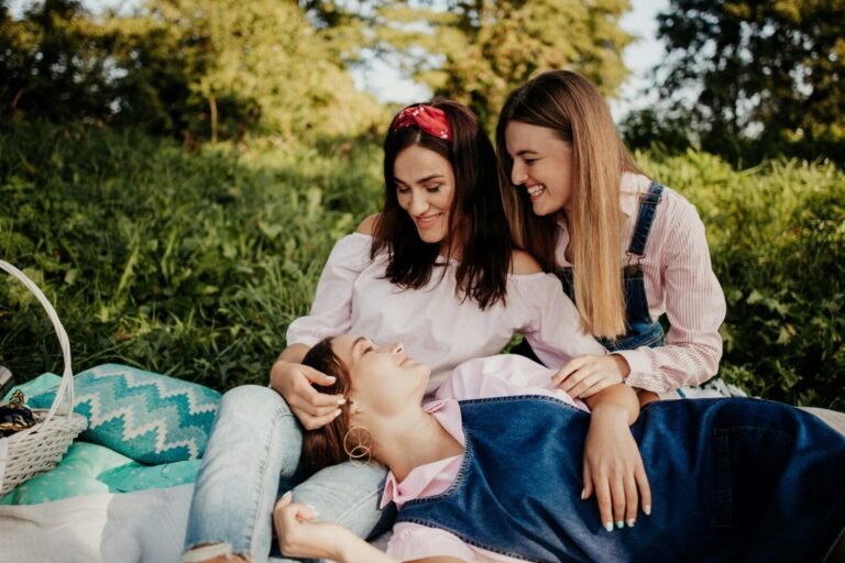 Three women enjoying a happy picnic outdoors in summer, laughing and relaxing together.