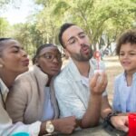 A joyful family bonding moment outdoors in a sunny park, blowing bubbles together.